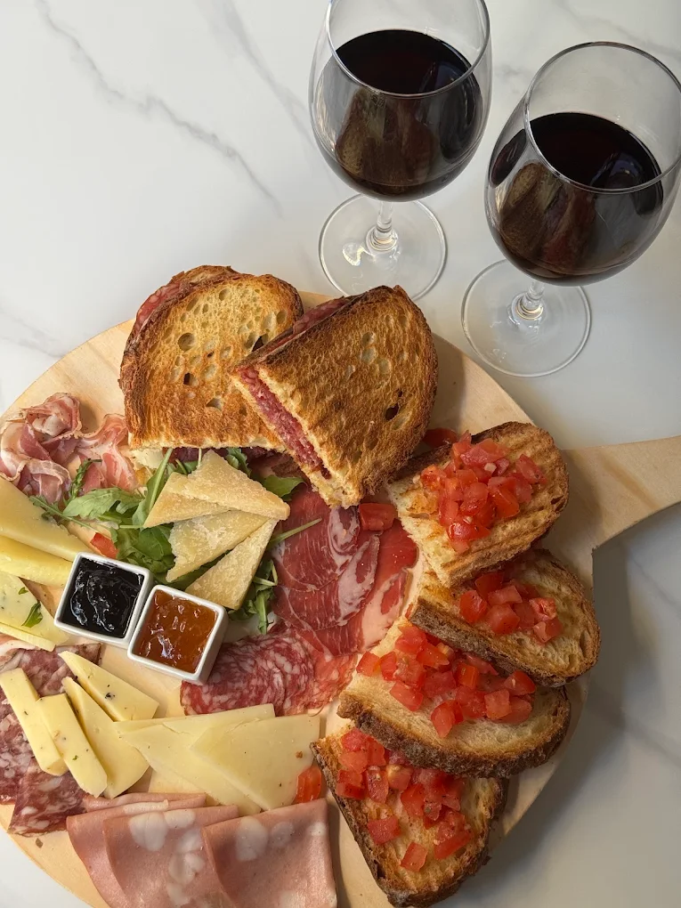 Tagliere di salumi, formaggi e bruschette al pomodoro con due calici di vino rosso